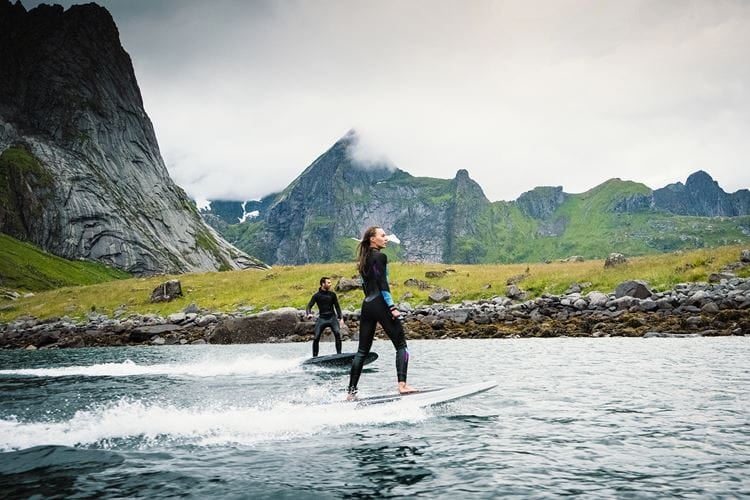 Two people standing on jetboards on water with mountains in the background