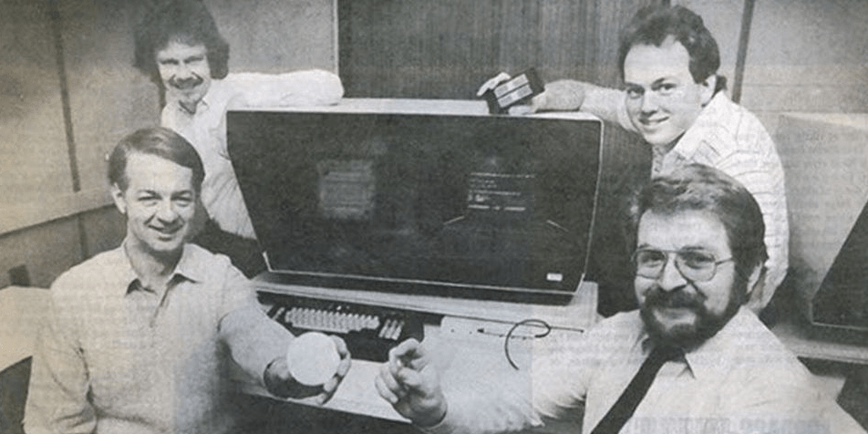 오래된 컴퓨터 주위에 앉아 있는 4명의 남자